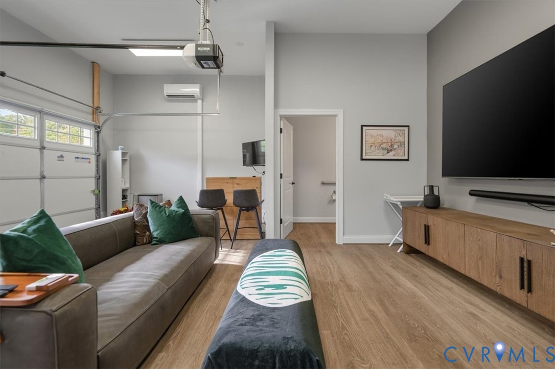 Finished Garage with half bath - Multi-functional room featuring wood-finish flooring, a mounted wall-unit mini-split HVAC system, a sectional overhead garage door, and neutral wall tones