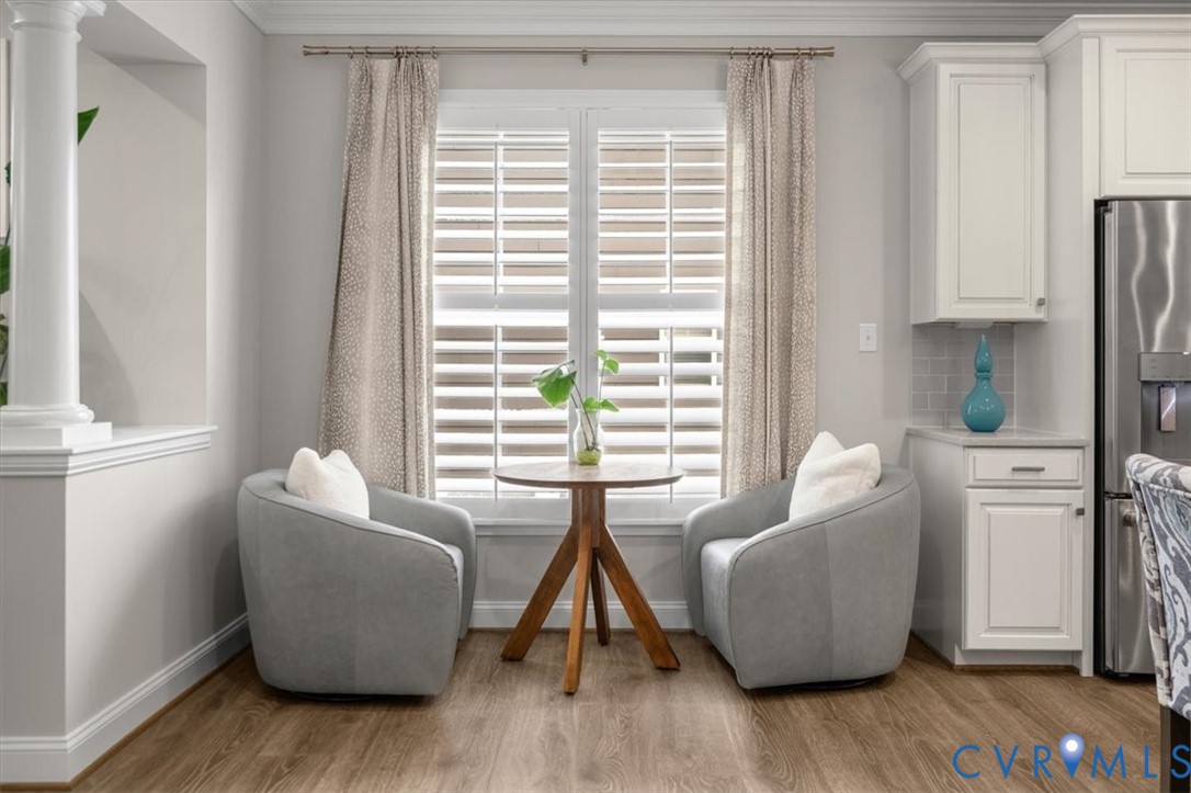 Wood-finish flooring, white shaker-style cabinetry, plantation shutters, and a decorative column
