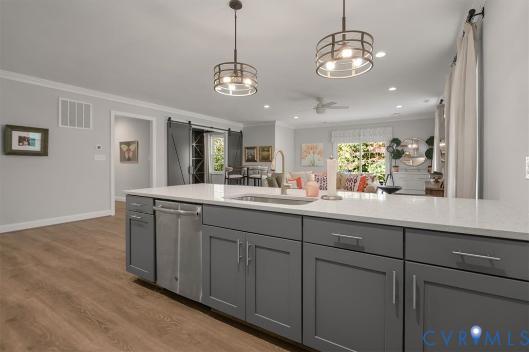 Terrace Level Kitchen island featuring a stone-composite countertop, undermount stainless steel sink, wood-finish cabinetry, and industrial-style pendant lighting, complemented by sliding barn-style doors