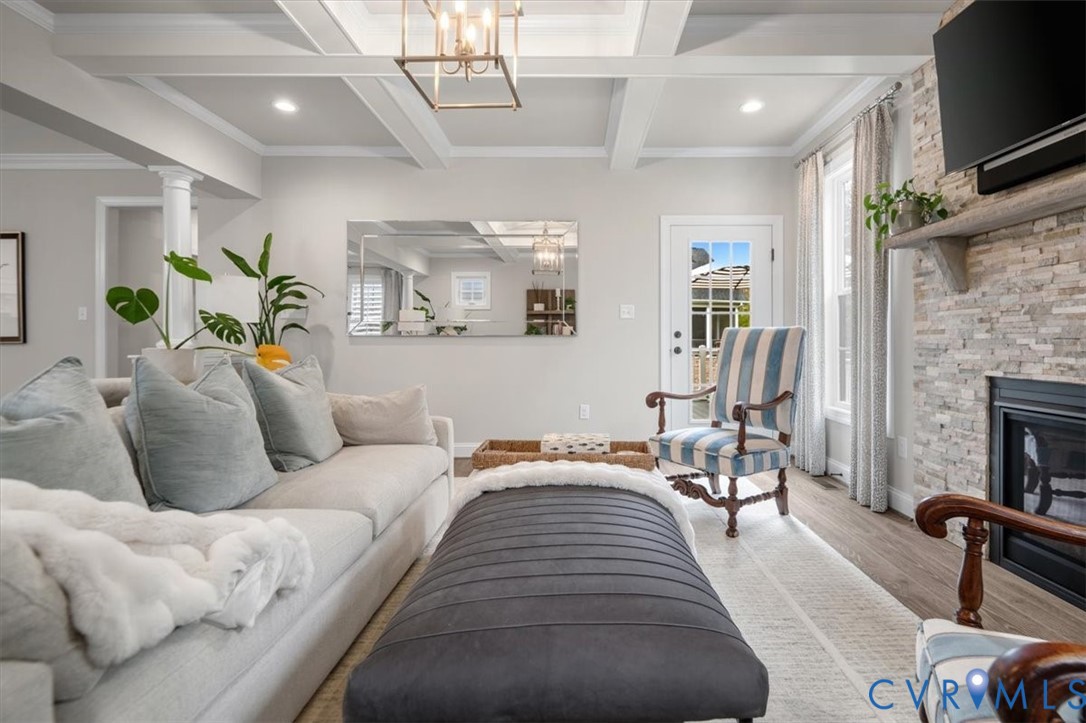 Coffered ceiling, stone-veneer fireplace with a wood mantel, wood-finish flooring, recessed lighting, and a lantern-style pendant light fixture