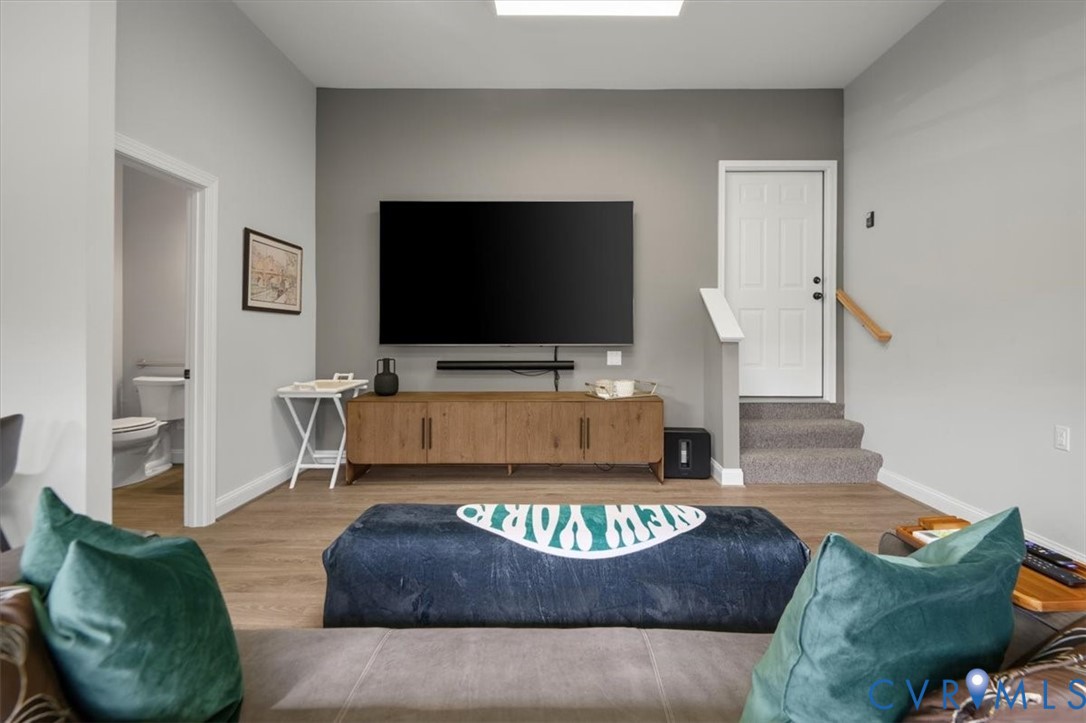 Finished Garage with half bath Living area featuring neutral wall tones, wood-finish flooring, a designated media wall, and carpeted stairs with a handrail