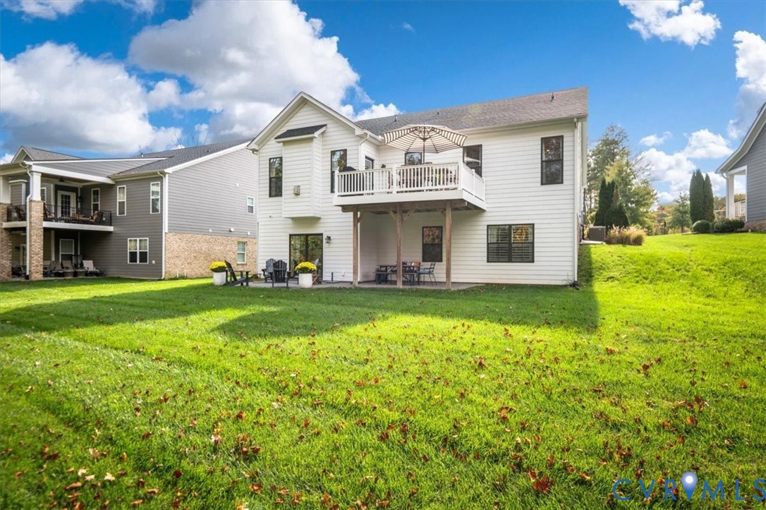 Rear exterior featuring white horizontal siding, an elevated wood deck, a ground-level concrete patio, and a grass lawn