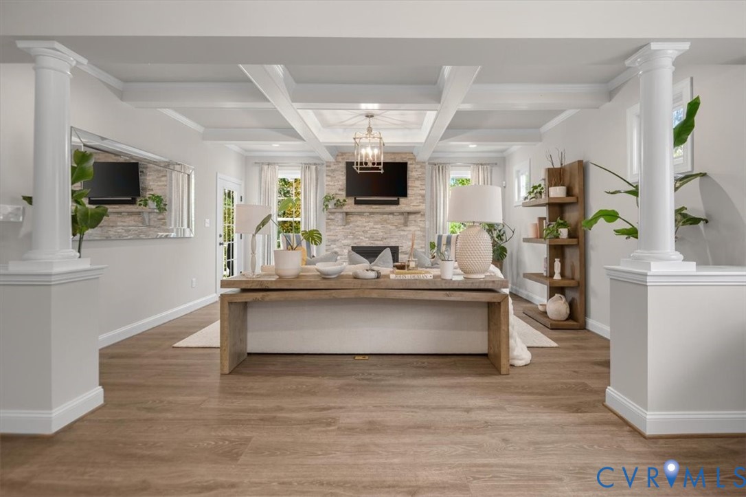Living area featuring coffered ceilings, stone-faced fireplace with wood mantel, wood-finish flooring, and decorative structural columns