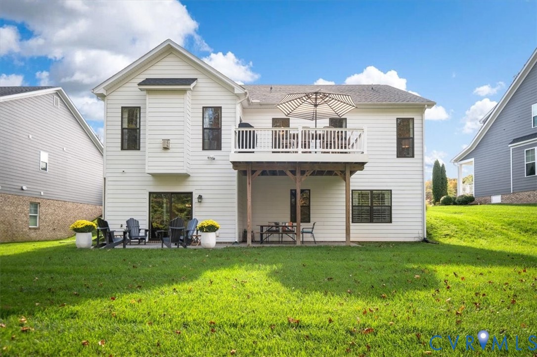 Rear exterior featuring horizontal lap siding, an elevated wood deck with white railings, a concrete patio, and a grass-covered lawn