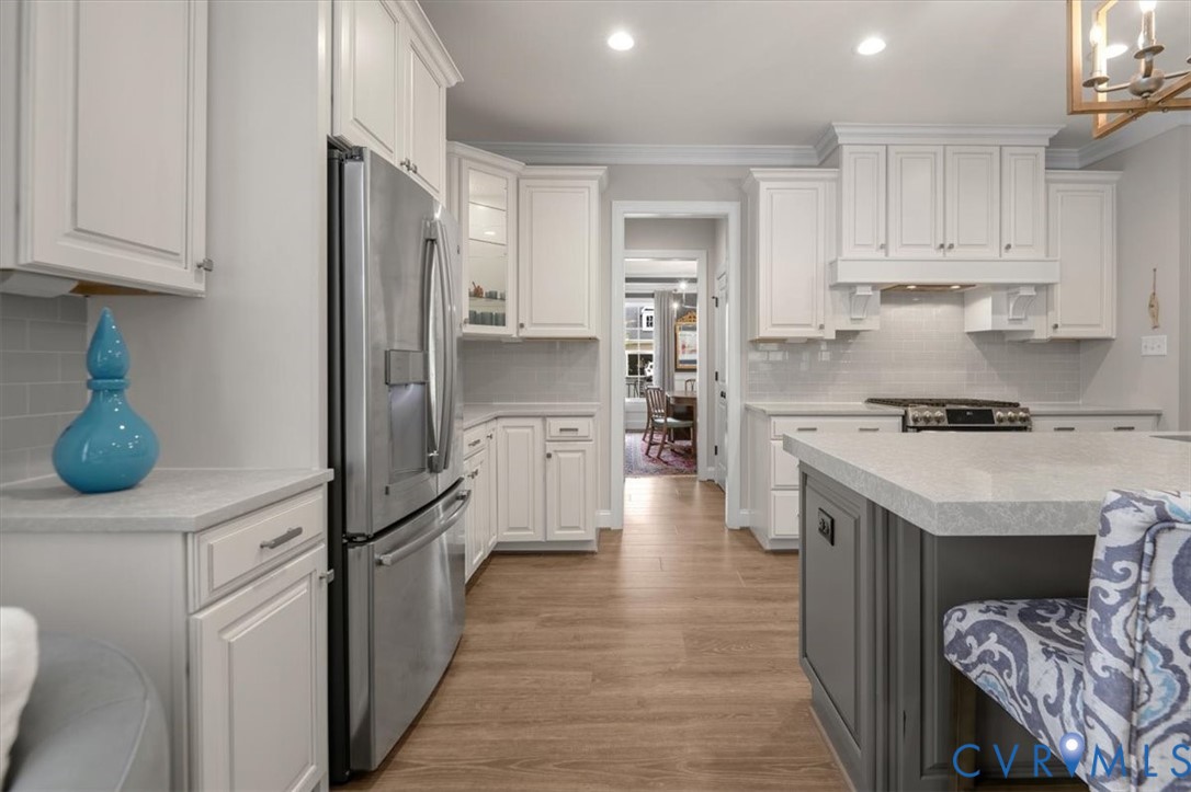 Kitchen featuring white cabinetry, center island with a stone-composite countertop, stainless steel appliances, tile backsplash, and wood-finish flooring