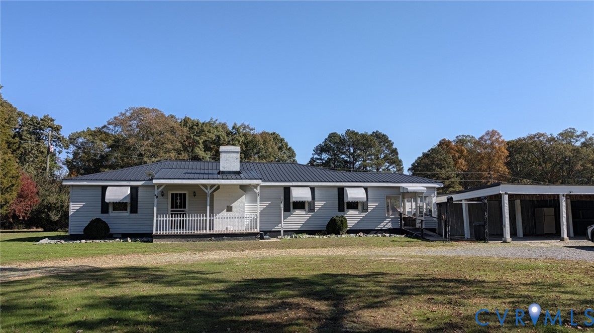 Single-story exterior featuring a metal roof, white siding, a covered front porch with railing, exterior shutters, and an attached carport