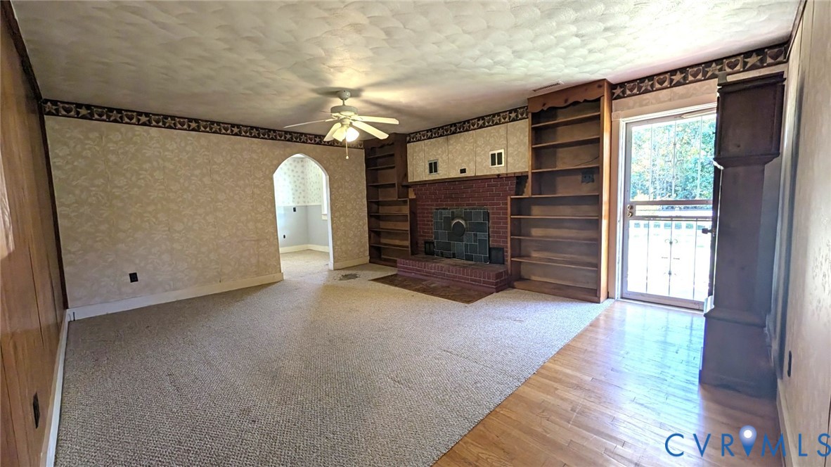Brick fireplace with integrated shelving, ceiling-mounted fan, arched doorway, and glass-paneled exterior door