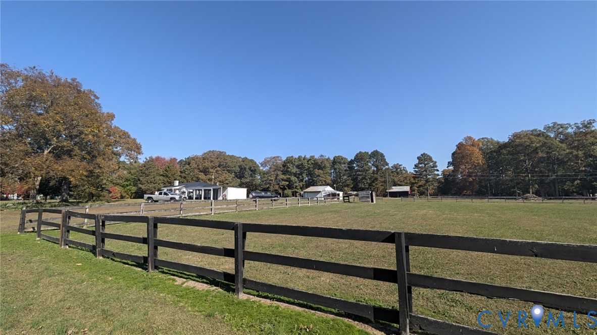 Expansive open pasture featuring post-and-rail fencing, multiple outbuildings, and mature tree growth