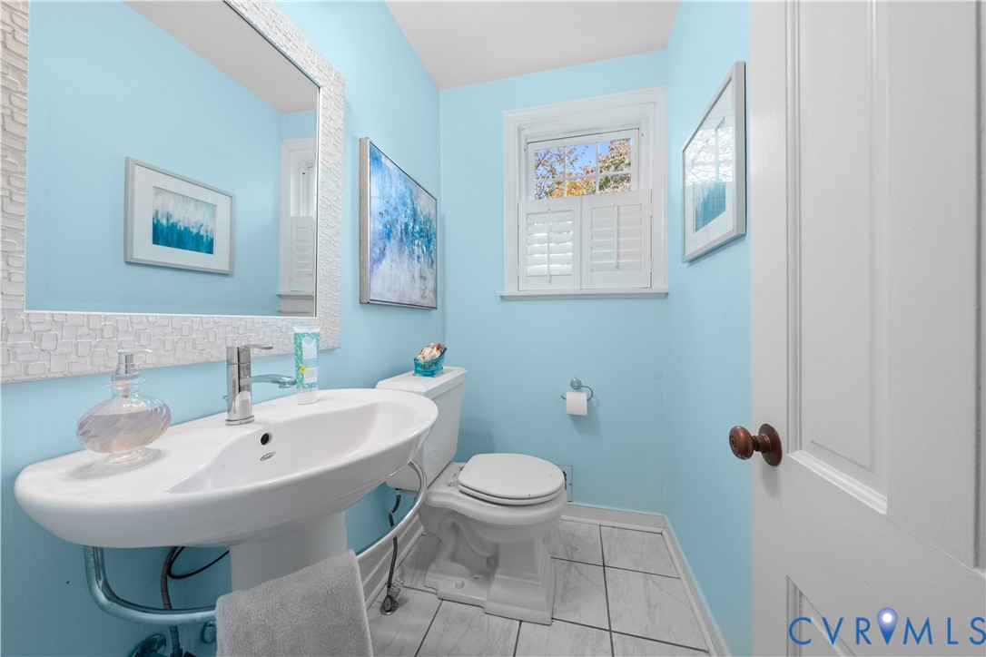 Powder room featuring a pedestal sink, polished chrome faucet, multi-pane window with plantation shutters, and tiled flooring