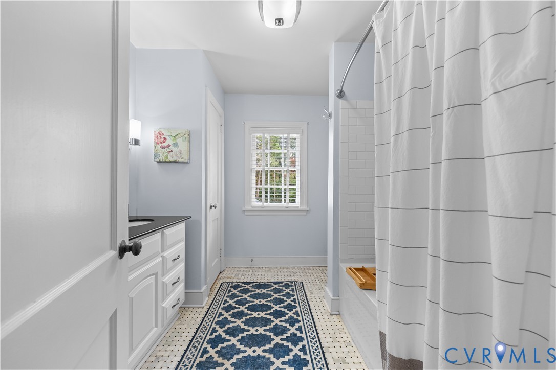 Bathroom featuring white cabinetry with a dark countertop, subway tile shower surround, patterned tile flooring, and a multi-pane window
