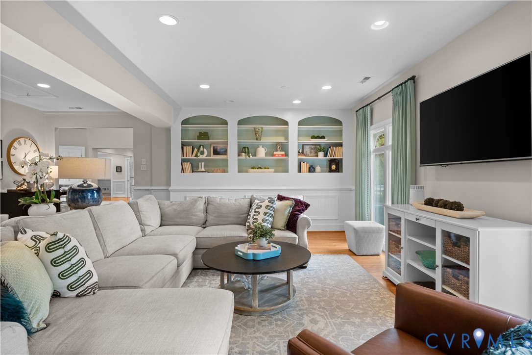 Living area featuring wood-finish flooring, recessed lighting, and triple arched built-in shelving with wainscoting