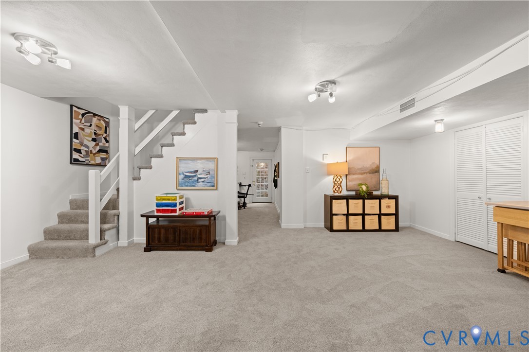 Open-concept interior space featuring wall-to-wall carpeting, staircase with wooden handrail, multi-light ceiling fixtures, and louvered double-door storage closet