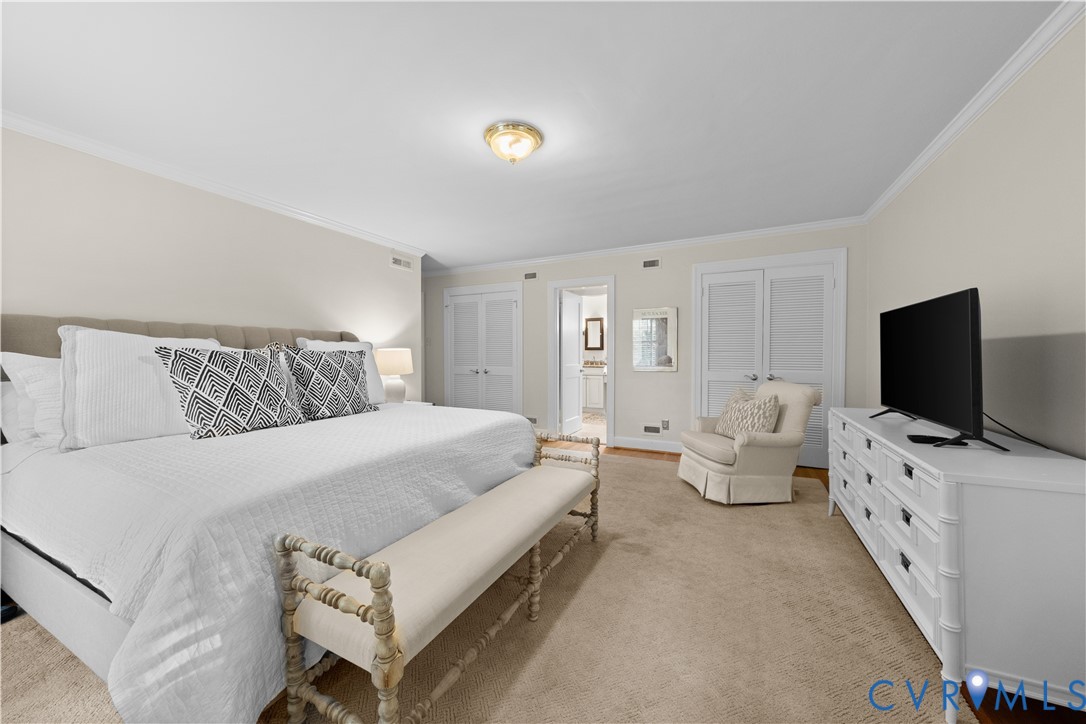 Neutral-toned bedroom featuring crown molding, carpeting, and dual-closet storage with louvered doors