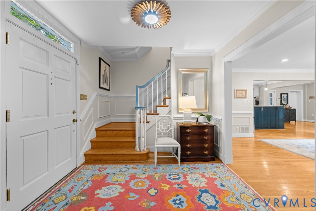 Entryway featuring a white paneled front door with transom window, wood-finish flooring, staircase with a white balustrade, wall wainscoting, and a decorative overhead light fixture