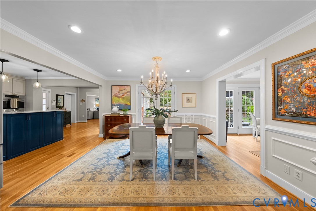 Dining space featuring wood-finish flooring, recessed lighting, ornate chandelier, wainscoting, and multi-light glass pane doors