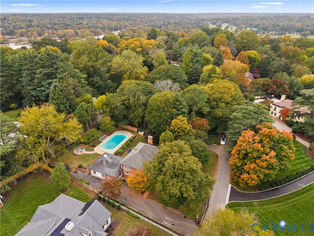 Aerial perspective featuring a multi-level residence, an inground swimming pool with a circular spa, mature tree canopy, and expansive grass lawns