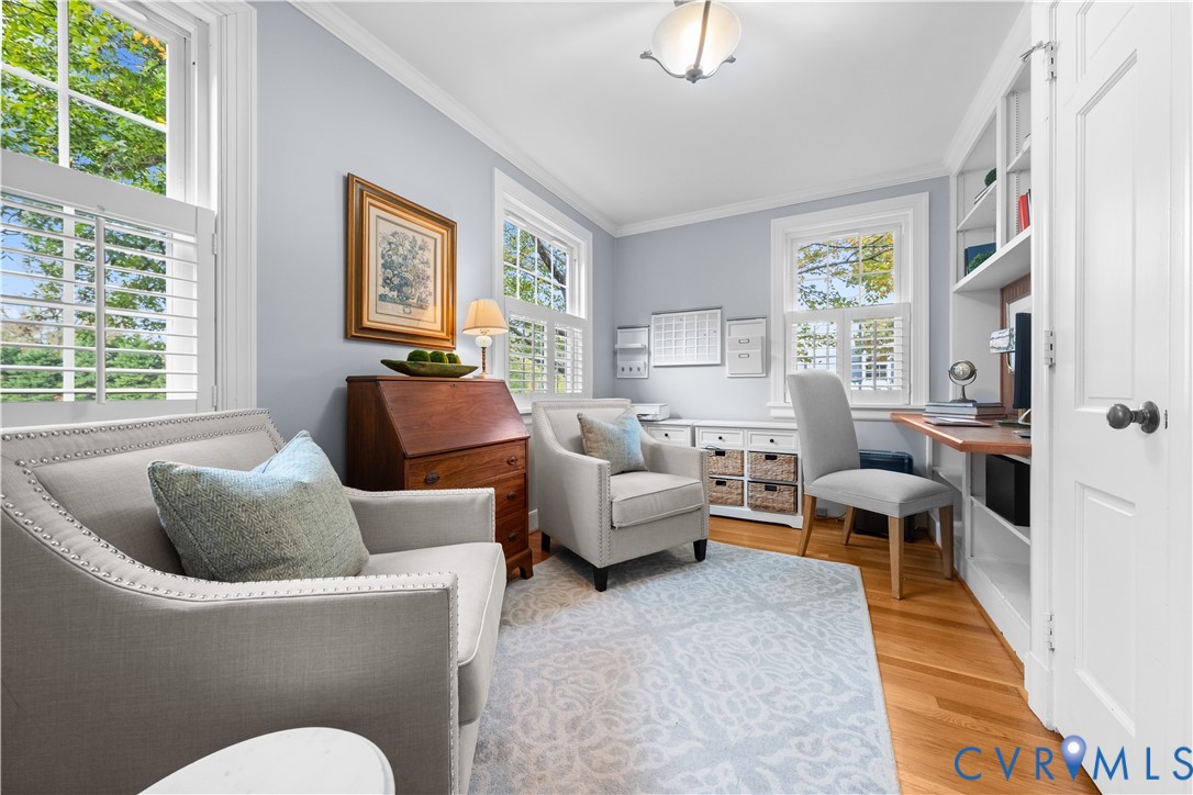 Multi-purpose room featuring wood-finish flooring, built-in shelving, a dedicated desk area, plantation shutters, and crown molding