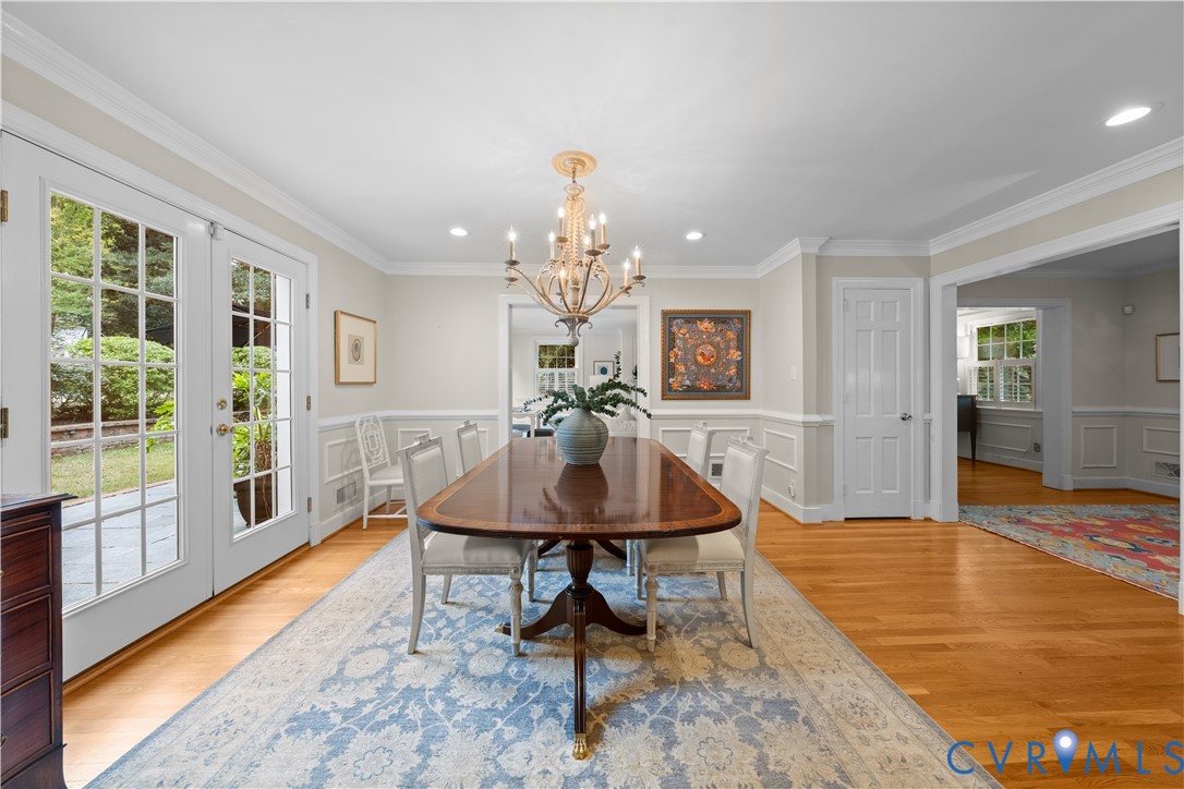 Dining area featuring wood-finish flooring, wainscoting, crown molding, a multi-arm chandelier, and double French doors