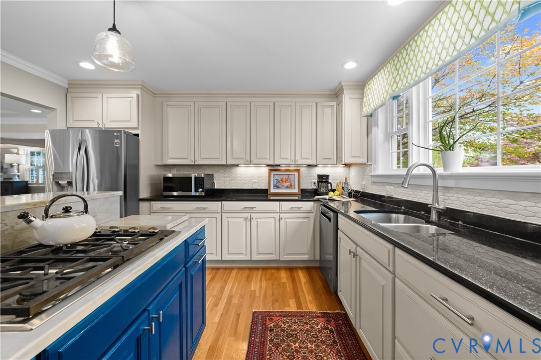 Kitchen featuring off-white cabinetry, dark stone countertops, wood-finish flooring, a blue-finished center island with an integrated cooktop, and stainless steel appliances