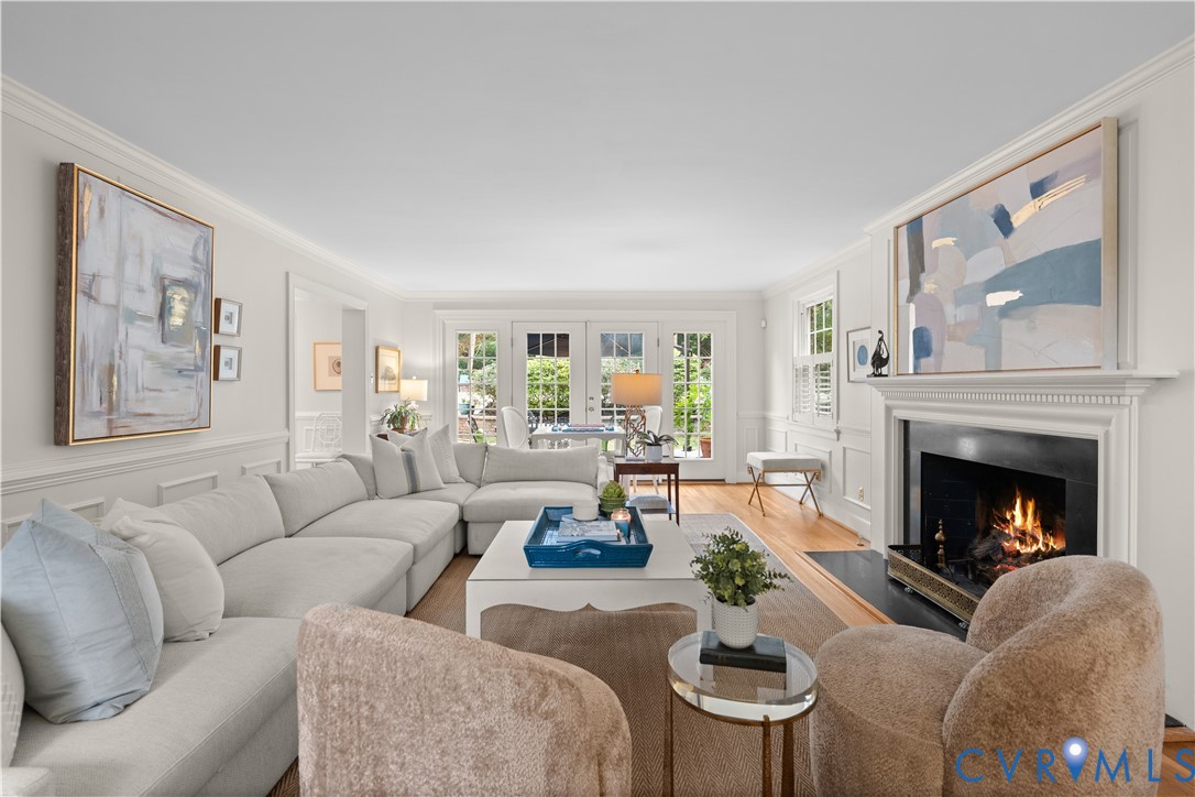 Living area featuring a fireplace with a traditional mantel and stone hearth, wood-finish flooring, wainscoting, and multi-pane glass doors