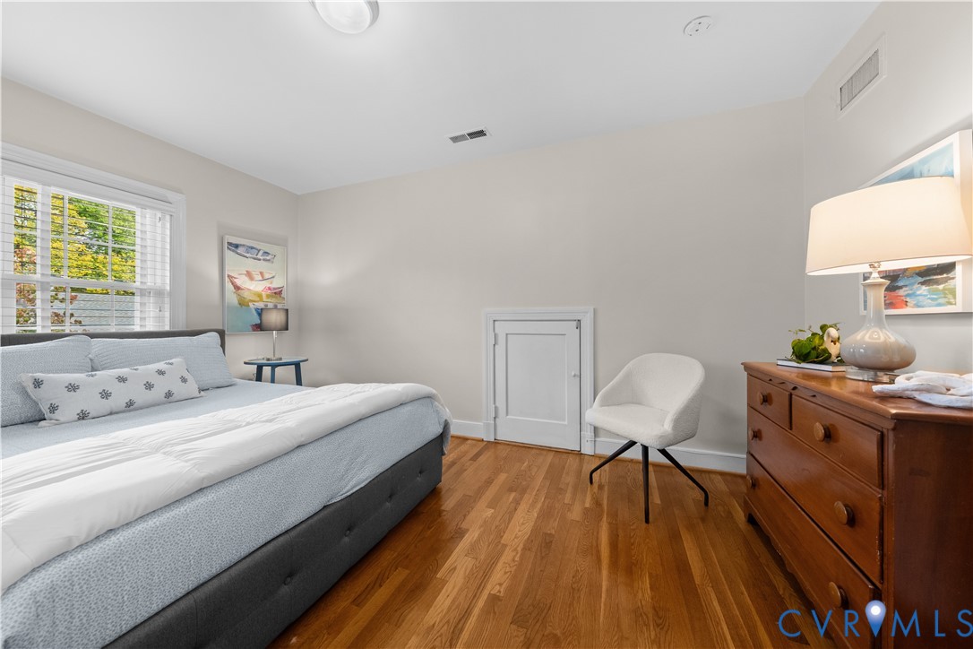 Bedroom featuring wood-finish flooring, neutral wall paint, multi-pane window with white trim, and built-in access panel