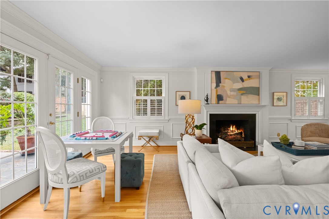 Wood-finish flooring, fireplace with a decorative mantel, crown molding, wainscoting, and multi-pane glass doors