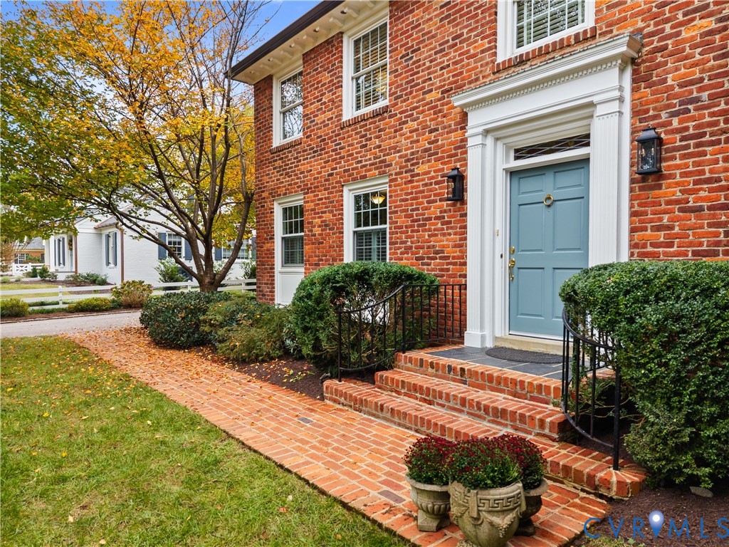 Traditional brick exterior featuring a classical architectural pediment over the entryway, multi-pane windows, a detailed transom, and a laid-brick walkway