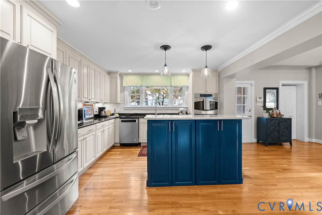 Kitchen featuring a central blue island, white shaker-style cabinetry, dark solid-surface countertops, wood-finish flooring, and stainless steel appliances
