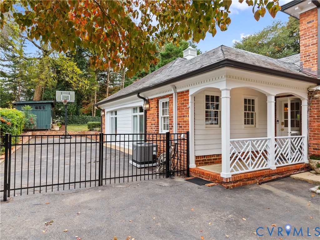 Brick and horizontal siding exterior featuring a covered porch with decorative wood lattice railing, dentil molding, and asphalt driveway with integrated metal fencing