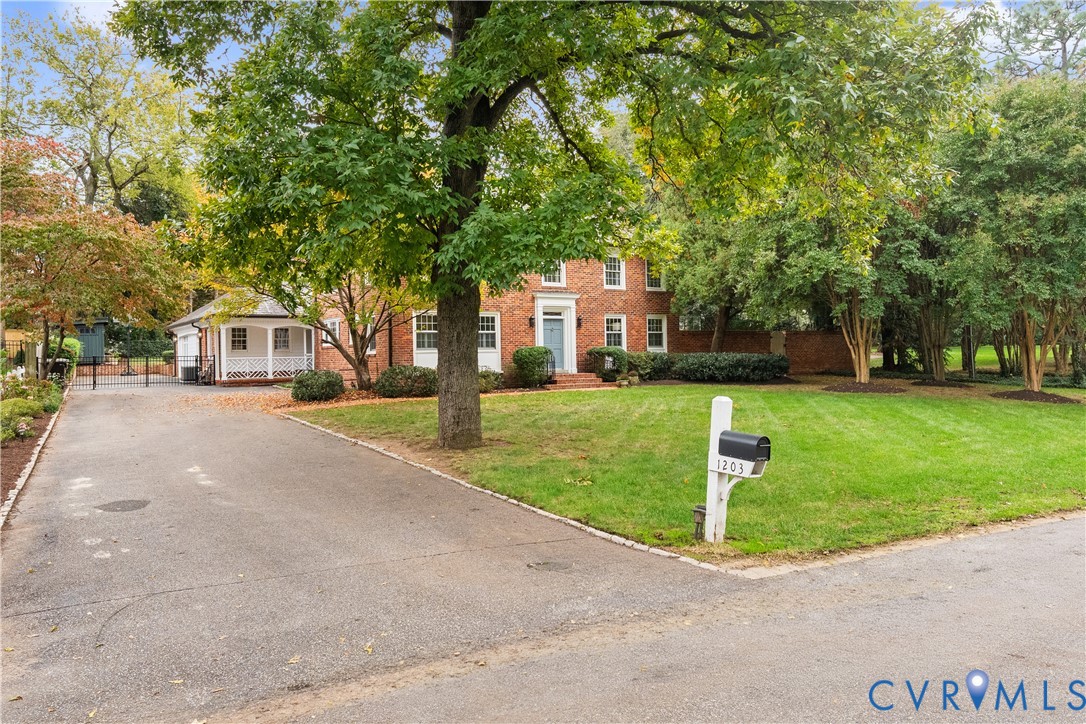 Two-story brick exterior featuring a covered porch, paved driveway, mature trees, and landscaping