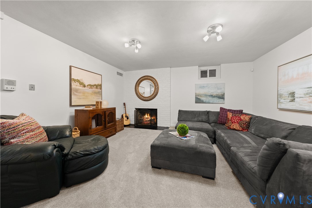 Interior space featuring a white painted brick fireplace, wall-to-wall carpeting, and multi-directional ceiling-mounted lighting