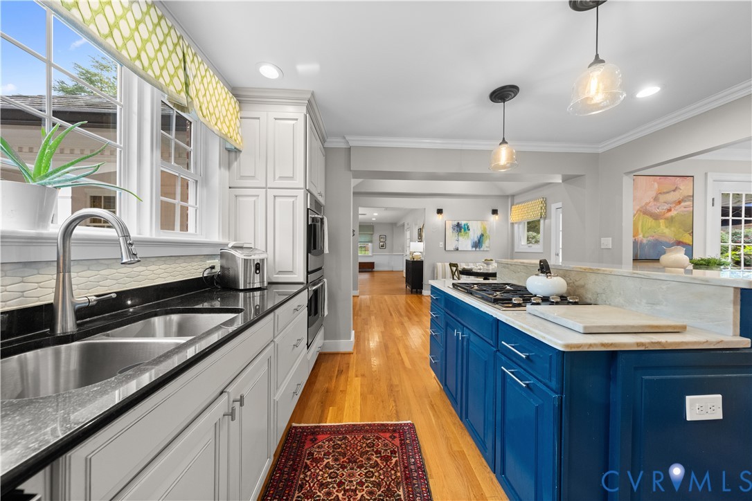Kitchen featuring white and deep blue cabinetry, stone countertops, stainless steel double-basin sink with arched faucet, built-in double wall oven, and wood-finish flooring