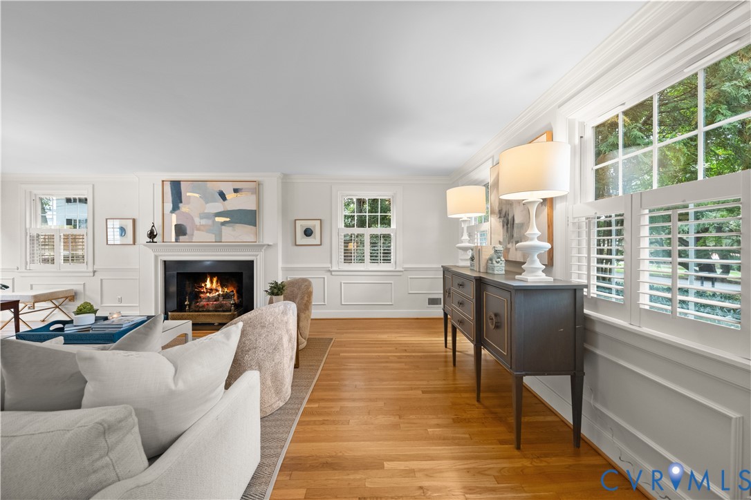 Wood-finish flooring, fireplace with a mantle, paneled wall molding, multi-pane windows with plantation shutters, and crown molding
