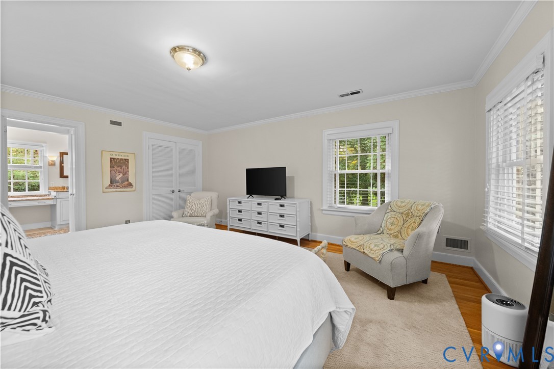 Bedroom featuring wood-finish flooring, crown molding, double-hung windows with horizontal blinds, and a double-door closet