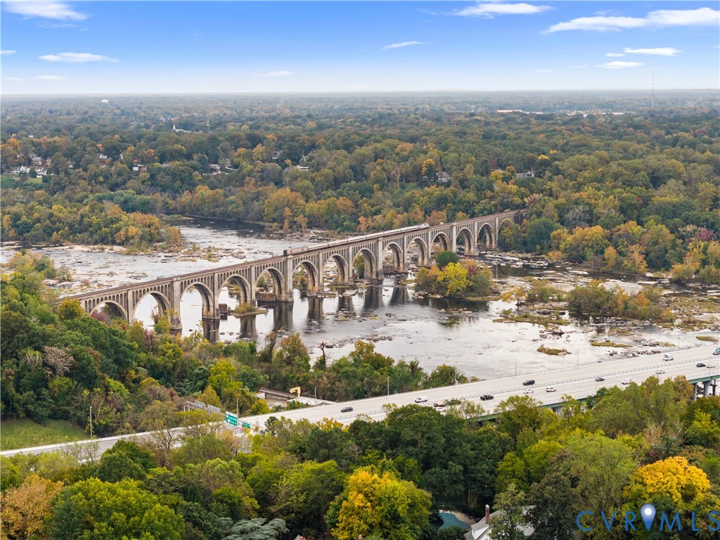 Aerial perspective featuring a river, mature forest canopy, and a stone arch bridge