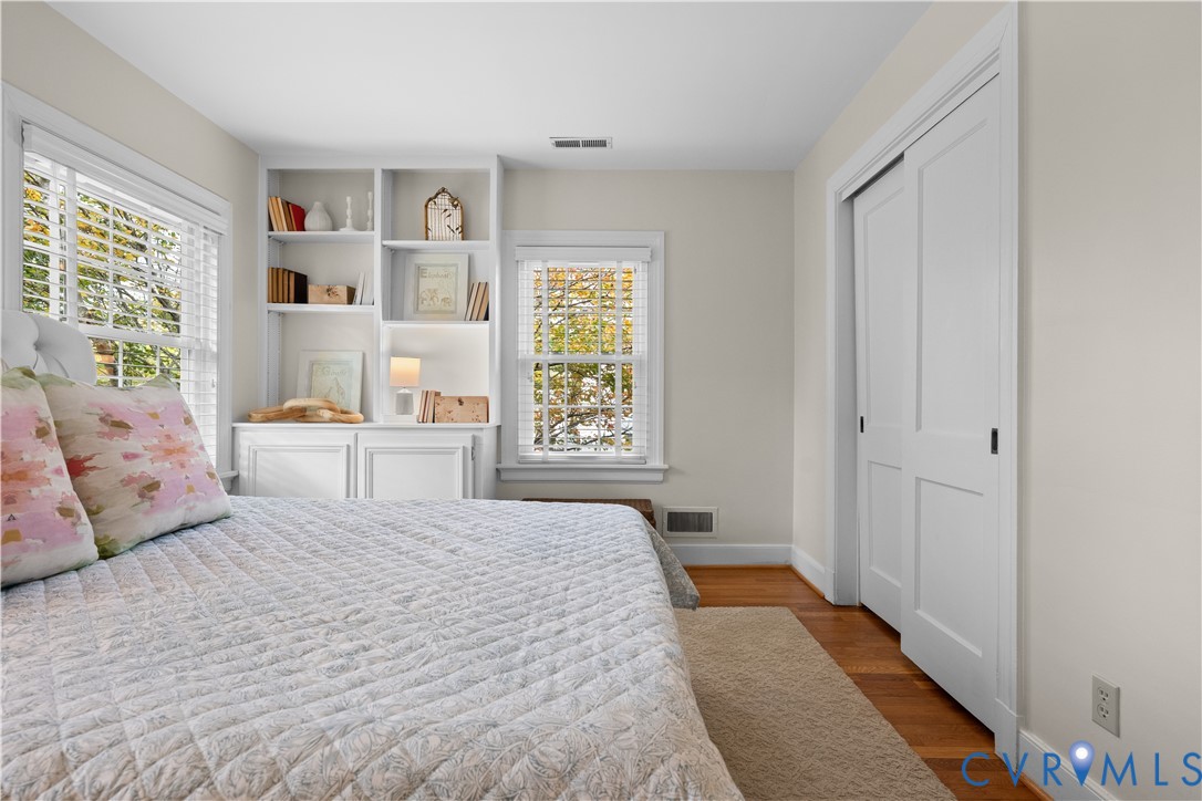 Built-in white shelving, wood flooring, multi-pane windows with horizontal blinds, and a dual-panel sliding closet door