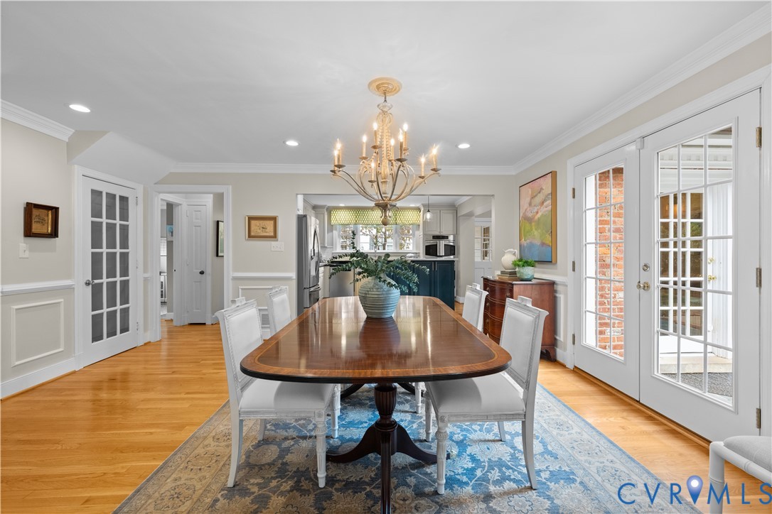 Dining area featuring wood-finish flooring, wainscoting, a decorative chandelier, and double glass-paneled exterior doors