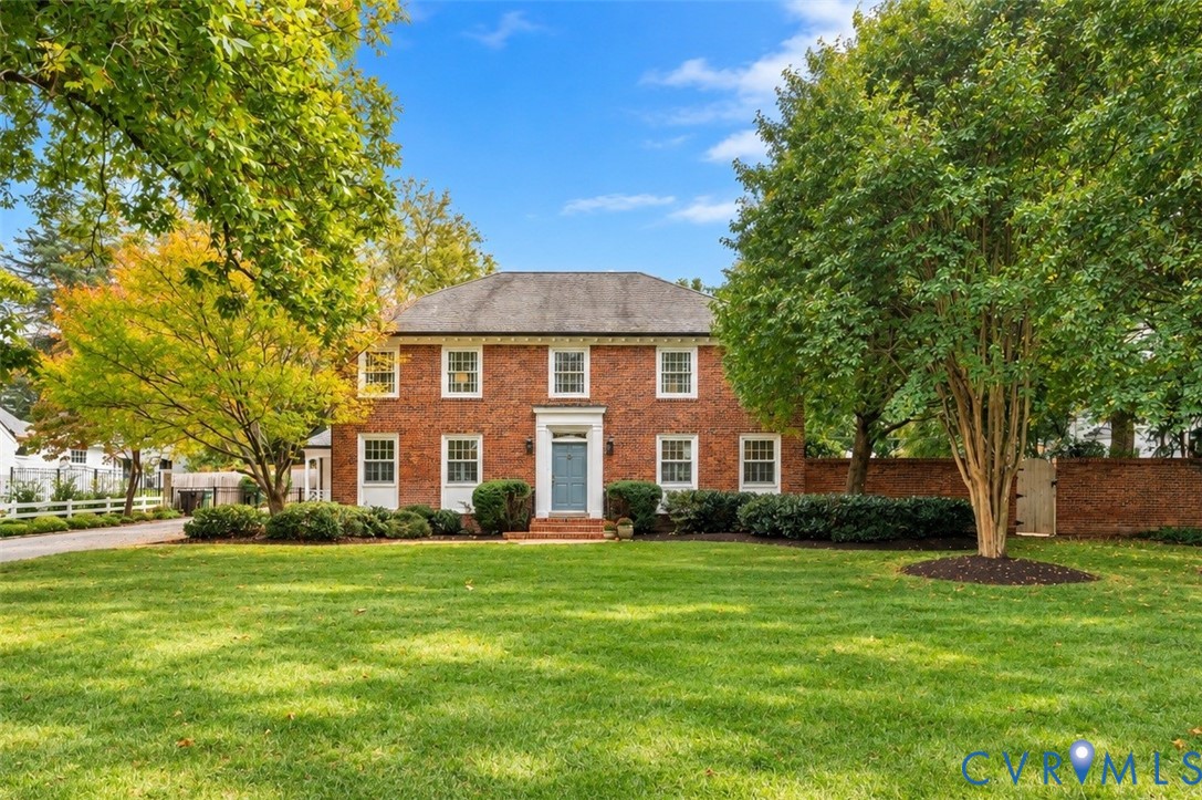 Two-story brick exterior featuring a multi-pane window configuration, a central entryway with transom light, a pitched roof, and a perimeter brick privacy wall