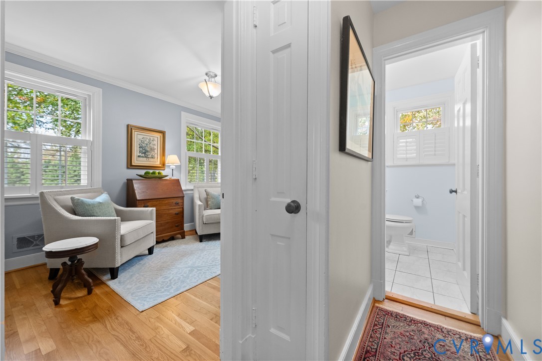 Room featuring wood-finish flooring, multi-pane windows with integrated shutters, and crown molding, with entry to a tiled bathroom