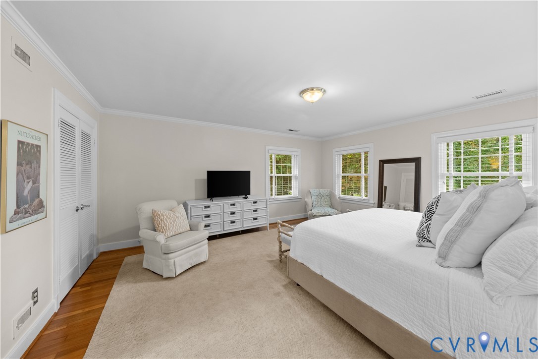 Spacious room featuring neutral carpeting, hardwood-finish flooring along the perimeter, white louvered-door closet, multi-pane windows with grids, and crown molding