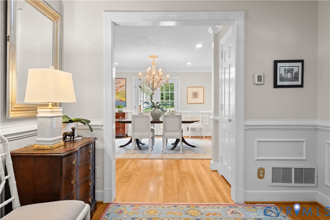 Neutral wall paint with chair rail molding, wood-finish flooring, and a formal chandelier