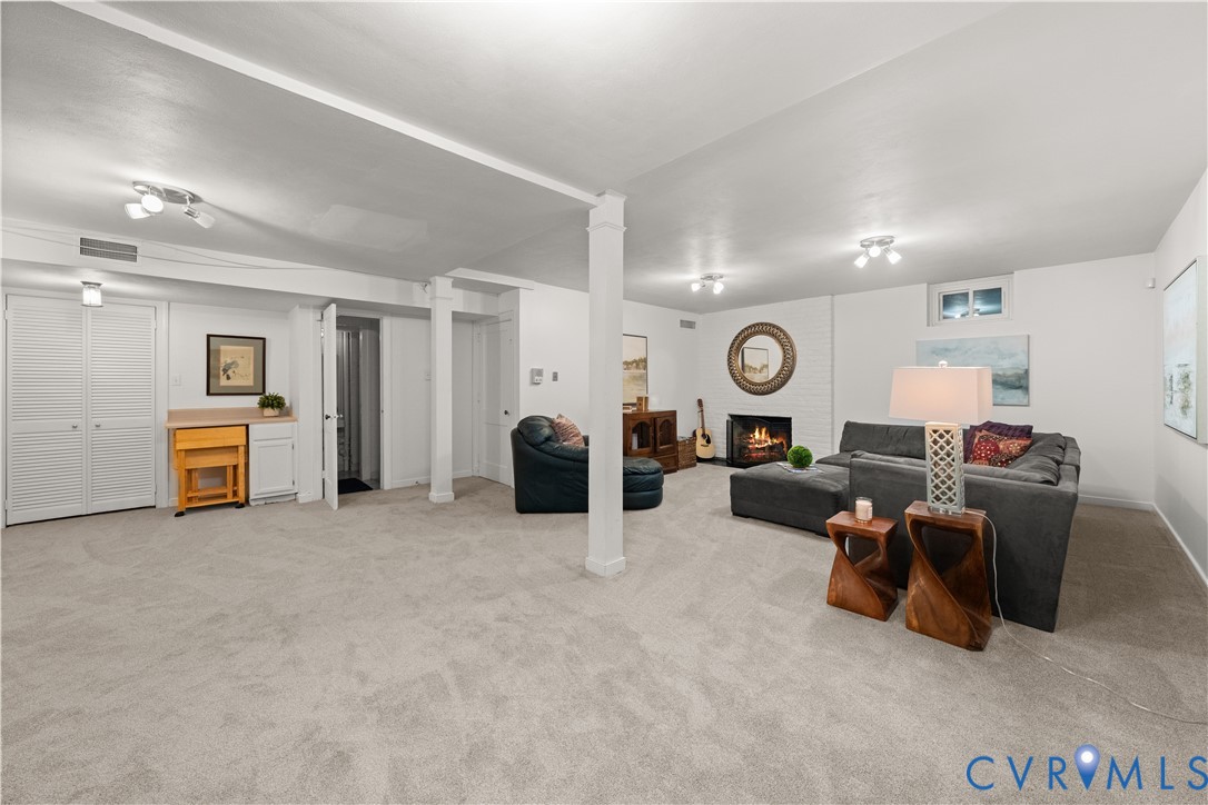 Spacious interior featuring neutral carpeting, a painted brick fireplace, built-in cabinetry, dual structural support columns, and recessed lighting