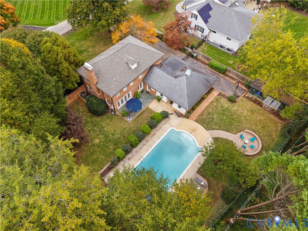 Brick exterior residence featuring an inground swimming pool, stone patio, circular hardscaped seating area, and established trees on the grounds
