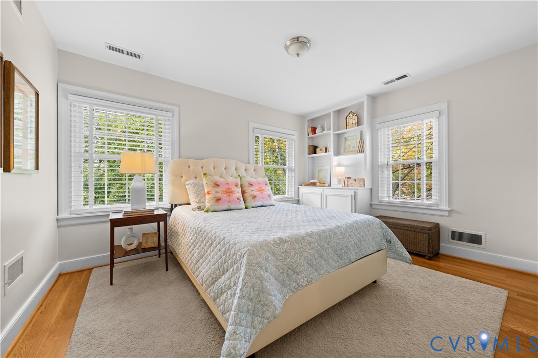 Neutral-toned room featuring hardwood flooring, built-in white shelving, and multiple windows with white wood-slat blinds
