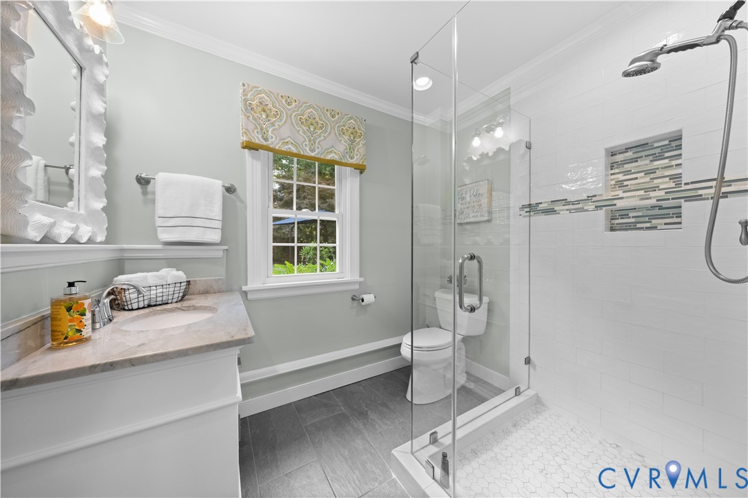 Bathroom featuring gray tile flooring, a stone-surfaced vanity with an integrated sink, a glass-enclosed walk-in shower with white subway tiling, and a recessed decorative tile niche
