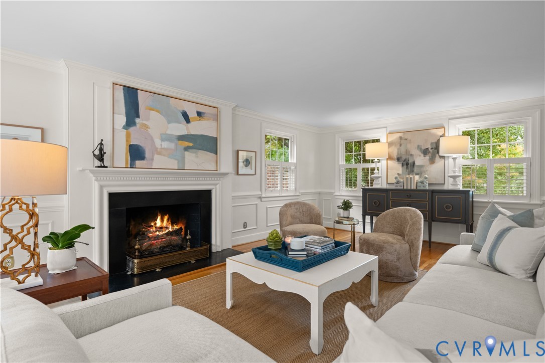 Living area featuring a fireplace with a detailed mantel, wainscoting, wood-finish flooring, and multiple windows with shutters