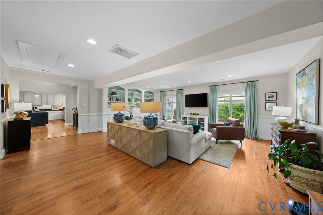 Living area featuring wood-finish flooring, custom built-in arched shelving, recessed lighting, and wall wainscoting