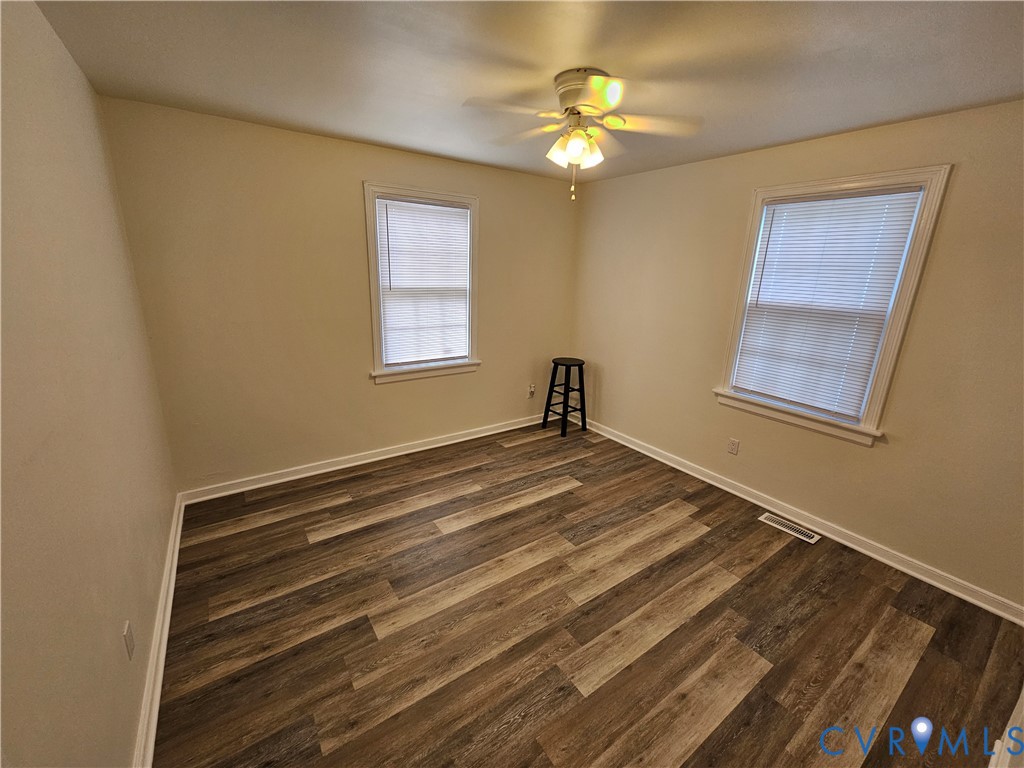 Neutral interior space featuring wood-finish flooring, two multi-pane windows, and a ceiling-mounted light fixture with integrated fan