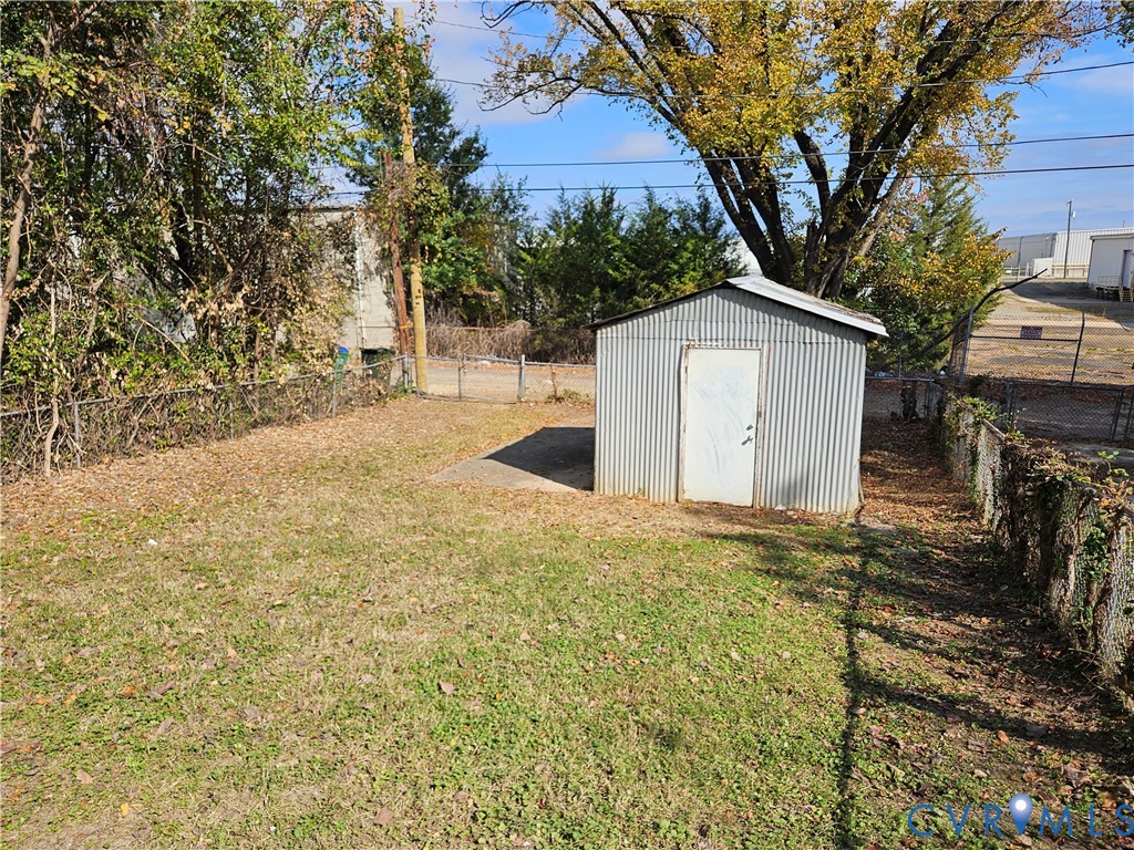 Rear yard featuring a corrugated metal storage shed, concrete pad, chain-link fencing, and mature trees
