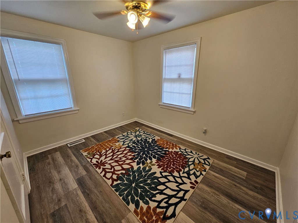 Interior room featuring wood-finish flooring, two dual-pane windows with horizontal blinds, and a ceiling-mounted light fixture with a central fan